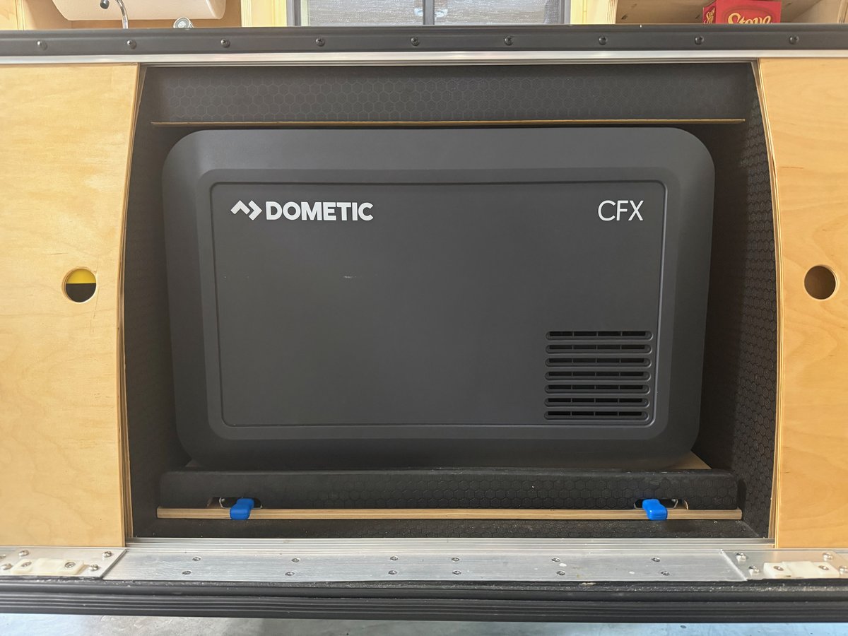 A Dometic CFX fridge closed in its galley bay under the counter, slide pushed home, with the release tabs visible under the tray