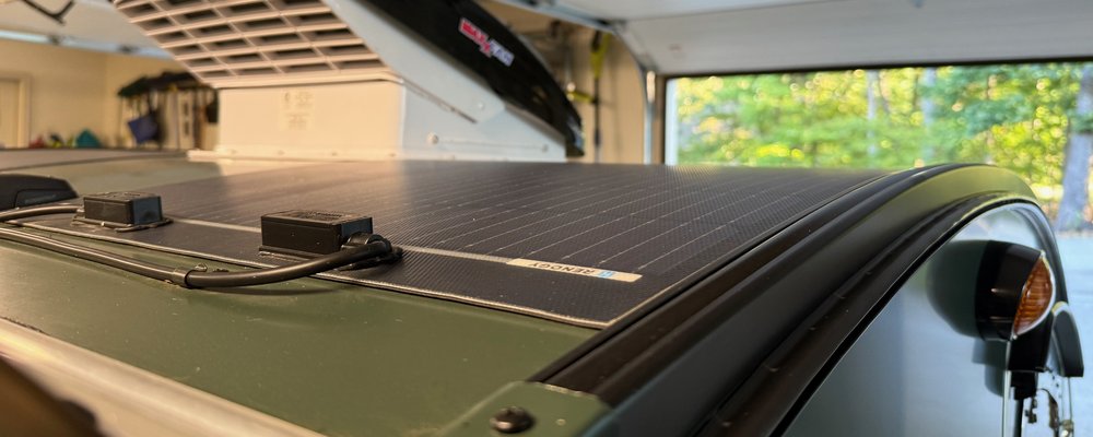 Low view along a teardrop camper roof as it curves down over the back, a flexible solar panel following the curve and a MaxxFan beyond