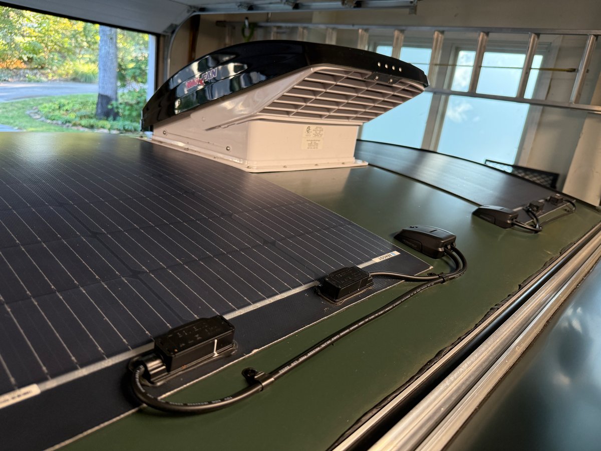 A flexible Renogy solar panel bonded to the green curved roof of a teardrop camper, with its junction boxes, a cable gland and a MaxxFan beyond it