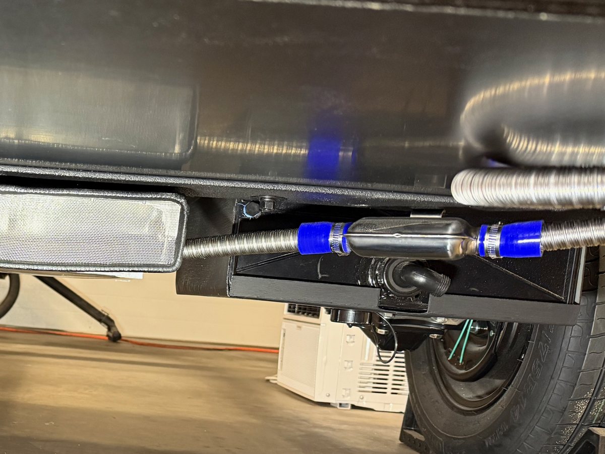 Stainless flexible exhaust pipe with an inline silencer and blue silicone couplers, run beneath a teardrop camper's floor