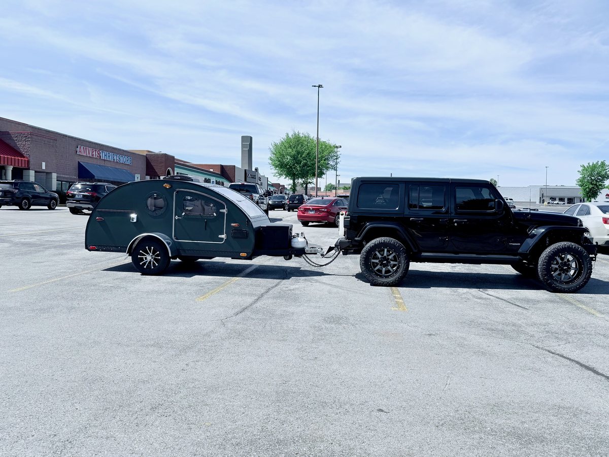 A black Jeep Wrangler hitched to a green teardrop camper in a parking lot, both sitting level